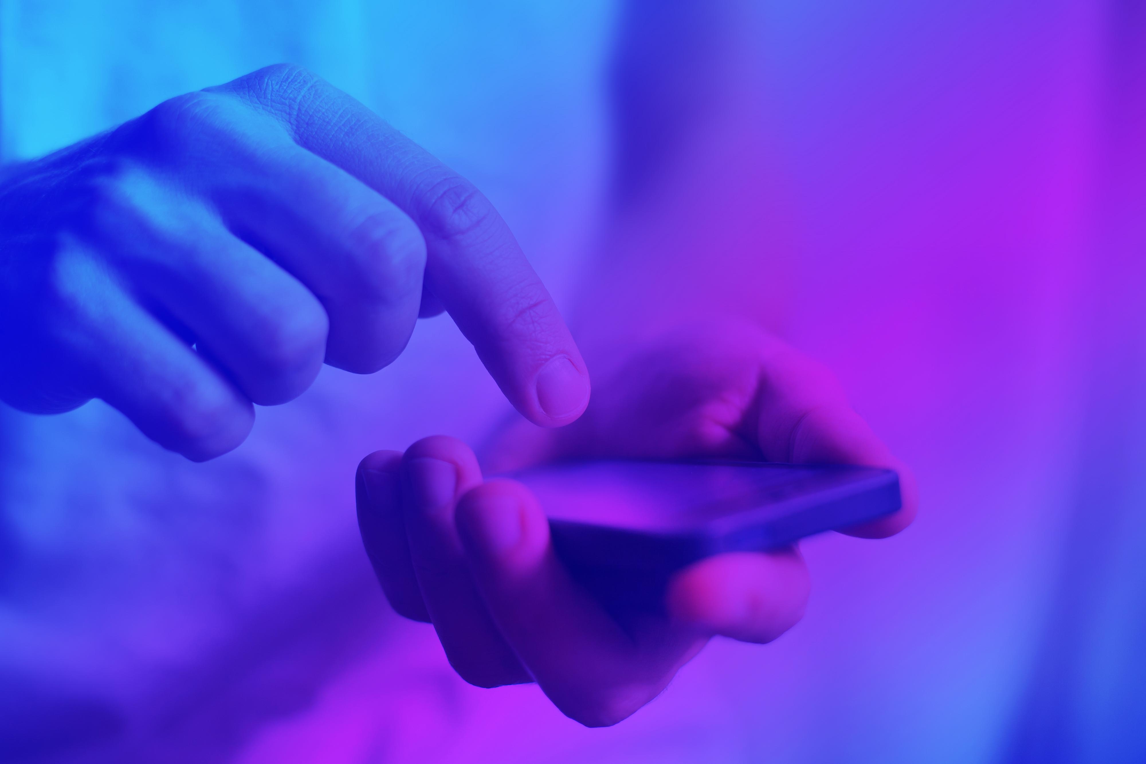Lähikuva käsiparista käyttämässä älypuhelinta violetissa valossa