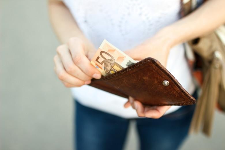 Girl is taking out a banknote of fifty euros from brown leather wallet on the street. Hands, money and wallet close-up