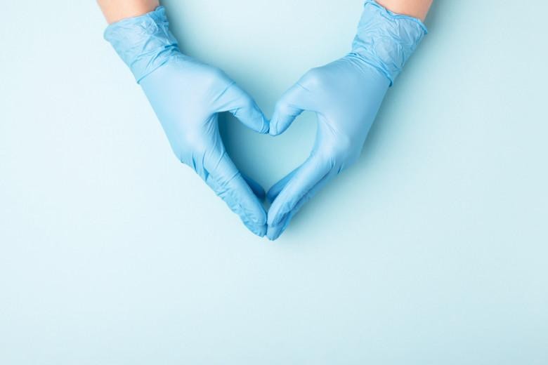 Doctor's hands in medical gloves in shape of heart on blue background with copy space.